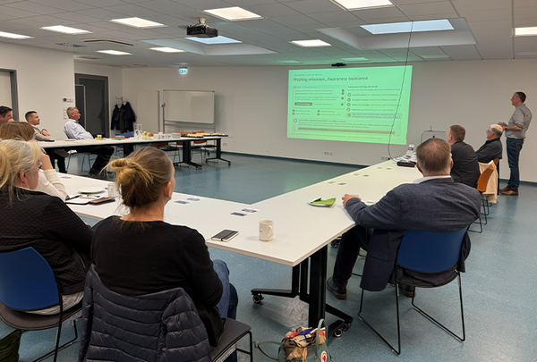 Tisch in U-Firm, Gäste des Unternehmerfrühstücks, Sven Schubbe, Bitburg IT GmbH, steht vor einer Wand und hält einen Vortrag, links von ihm Projektion der Präsentation
