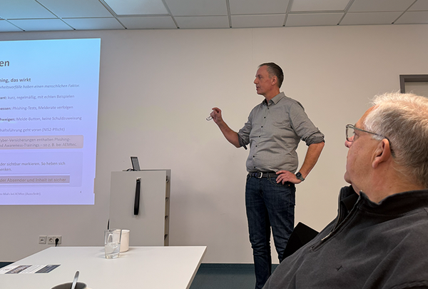 Sven Schubbe, Bitburg IT GmbH, steht vor einer Wand und hält einen Vortrag, links von ihm Projektion der Präsentation